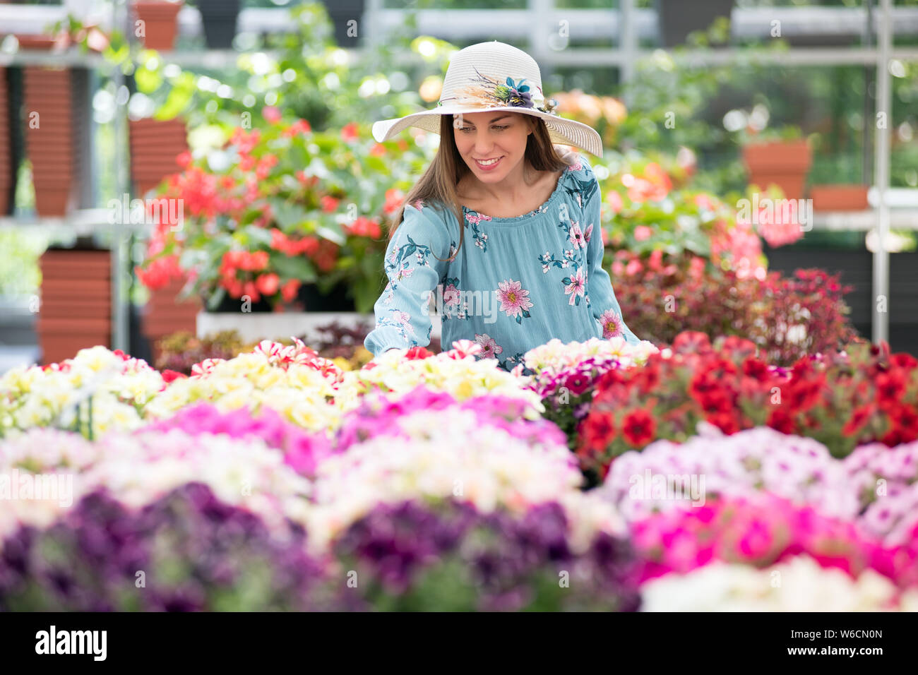 Junge Frau in Sonnenhut kaufen Bunt blühende Pflanzen im Sommer ein Kindergarten, eine Auswahl aus einer großen Array auf der Anzeige Stockfoto
