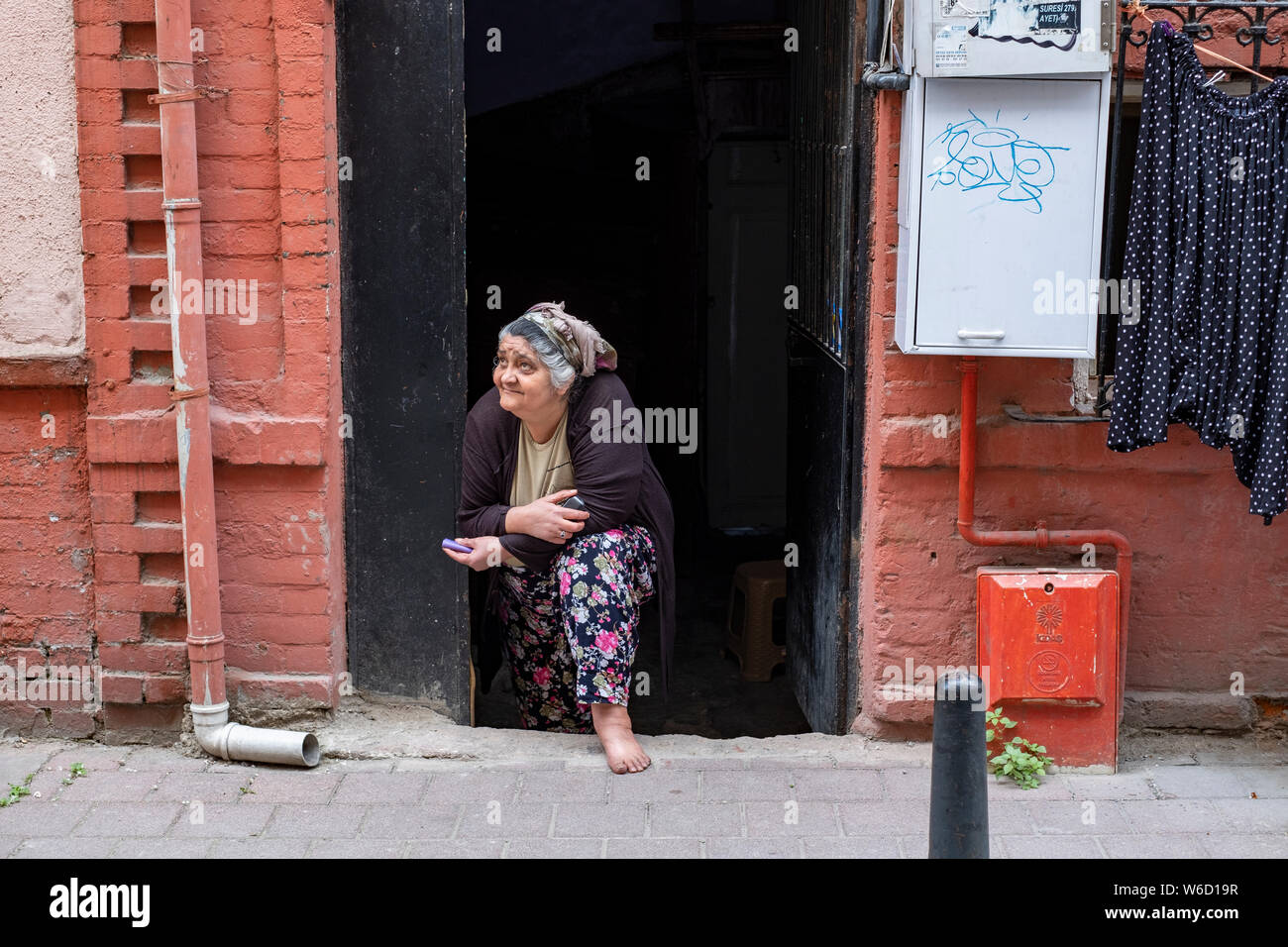 Eine ältere türkische Frau mit Kopftuch Umfragen die Aktivität auf der Straße vor ihrem Haus im Zentrum von Istanbul, Türkei Stockfoto