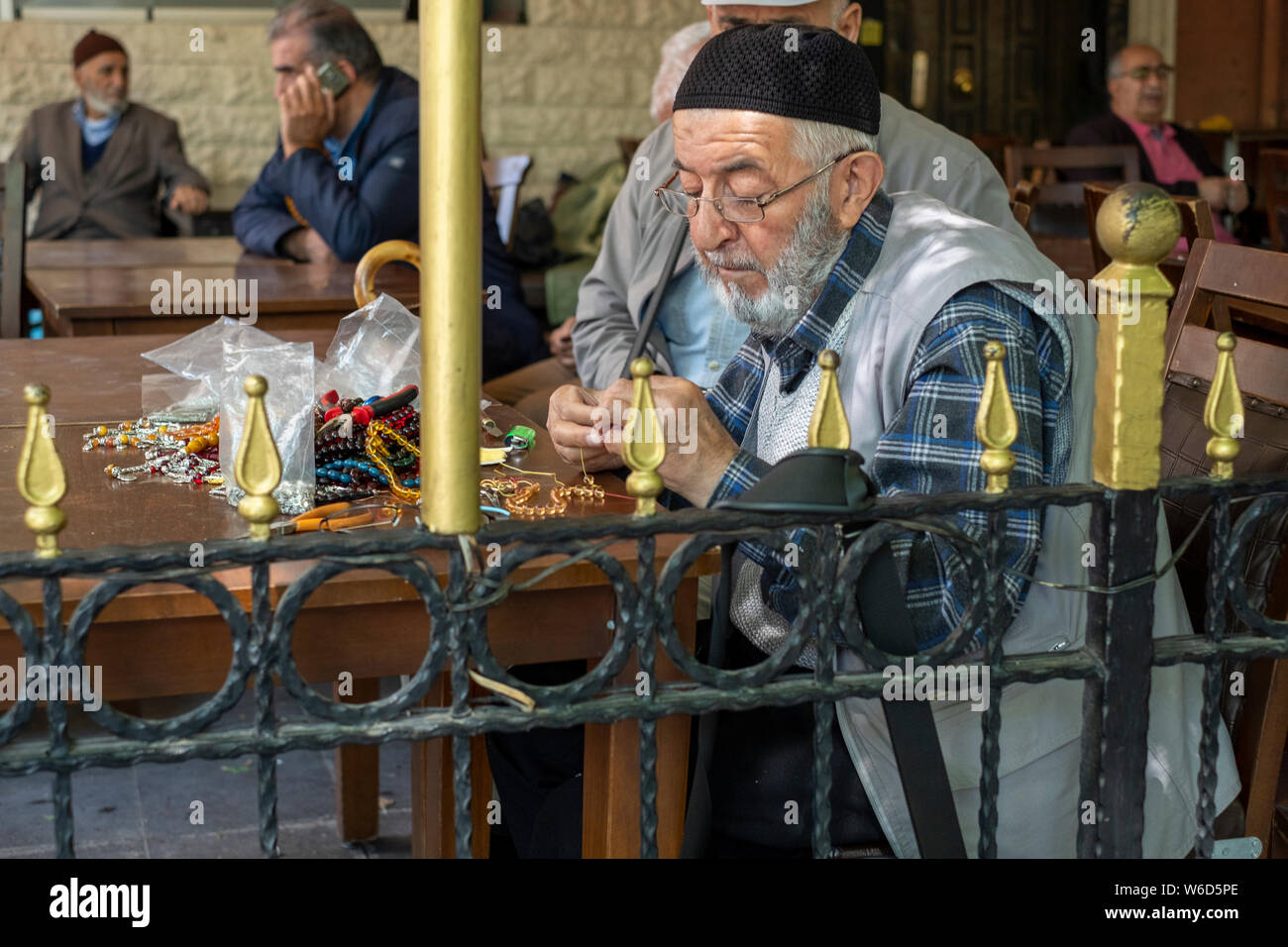 Ein älterer Mann in einen Hut und Weste Handwerk sorgen, Perlen und Ketten auf einem Cafe Tabelle im Zentrum von Istanbul, Türkei Stockfoto