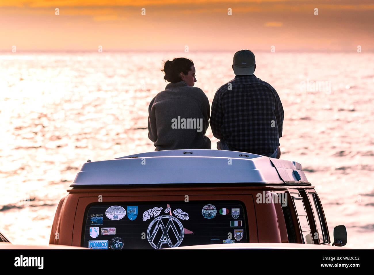 Urlauber sitzen auf ihren VW Volkswagen Wohnmobil einen spektakulären Sonnenuntergang auf den Fistral in Newquay in Cornwall. Stockfoto