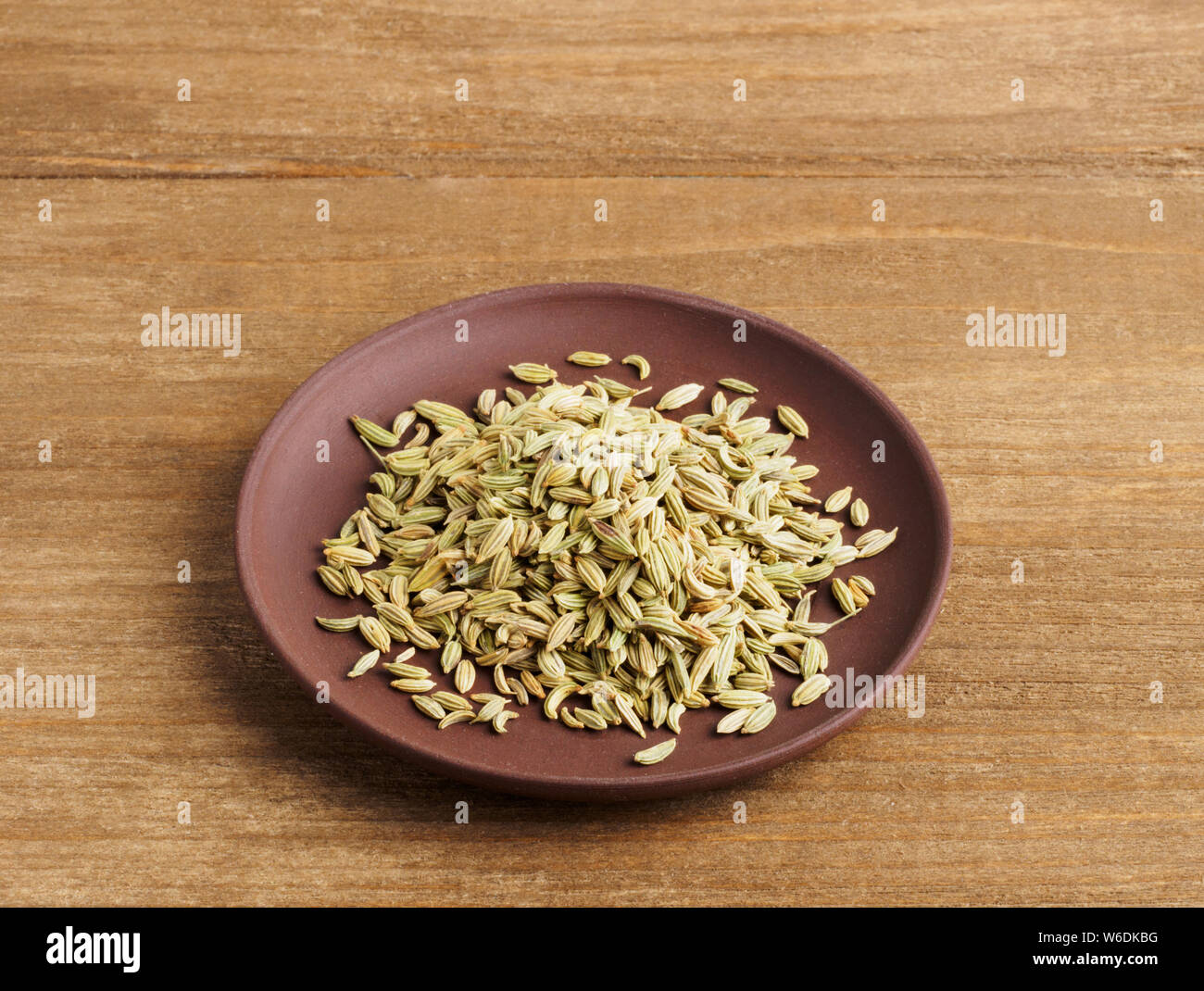 Fenchel (Foeniculum vulgare) Samen in ein Ton Platte auf einem hölzernen Hintergrund Stockfoto