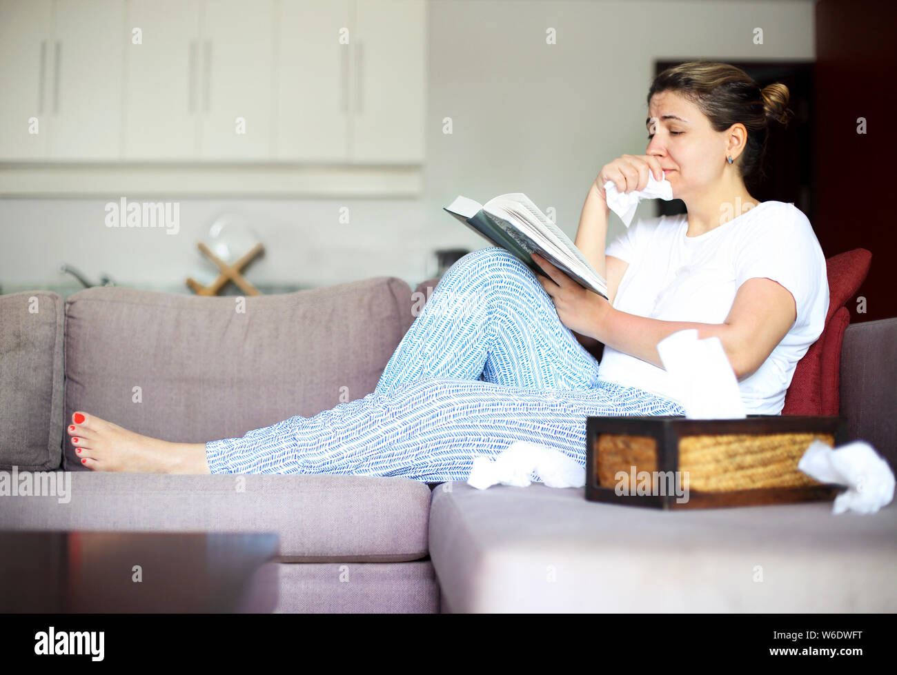 Traurige Frau, das Buch zu lesen Holding Papier Servietten auf dem Sofa sitzt. Stockfoto