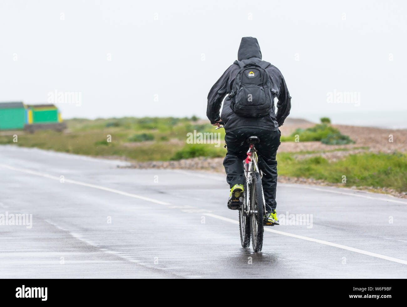 Mann reiten Fahrrad entlang der Strandpromenade auf einer schlechten Wetters nassen Tag bei Regen. Stockfoto