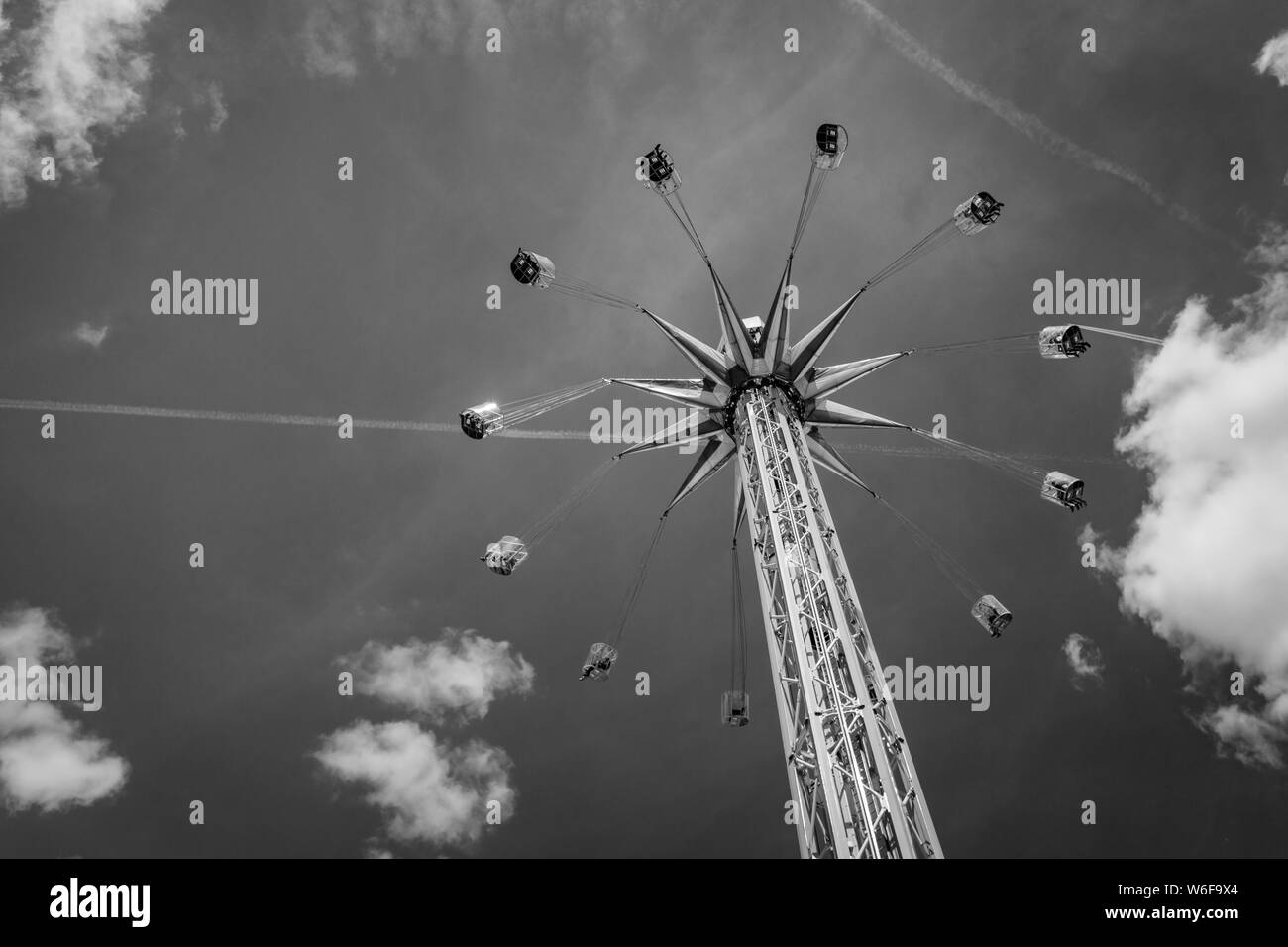 Schwarz-weiß Bild von Fahrgeschäft auf chairoplane mit fliegenden Menschen vor einem teilweise bewölktem Himmel Stockfoto