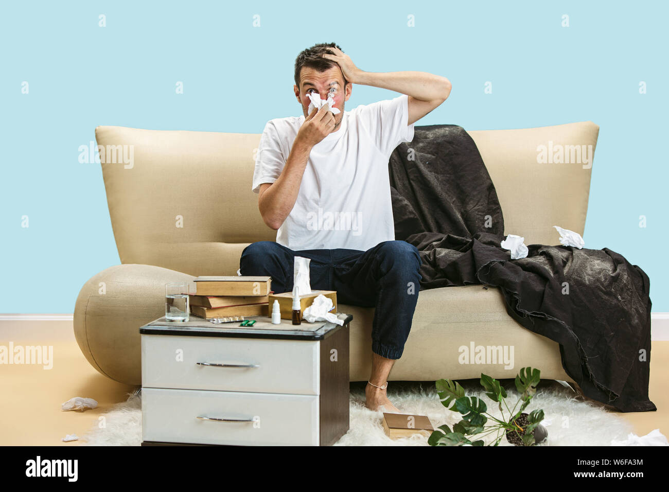 Junge Menschen leiden unter hausehold Staub oder saisonale Allergien und Kopfschmerzen. Niesen in die Serviette, die von gebrauchten Servietten auf dem Boden umgeben. Arzneimittel ohne Ergebnis. Healthcare Konzept. Stockfoto