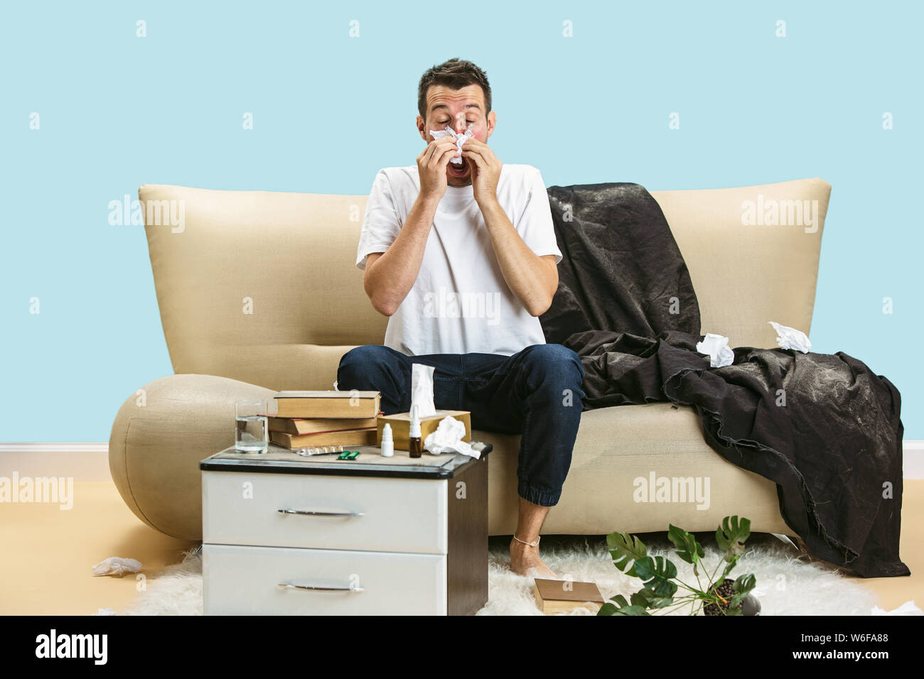 Junge Menschen leiden unter hausehold Staub oder saisonale Allergien und Kopfschmerzen. Niesen in die Serviette, die von gebrauchten Servietten auf dem Boden umgeben. Arzneimittel ohne Ergebnis. Healthcare Konzept. Stockfoto