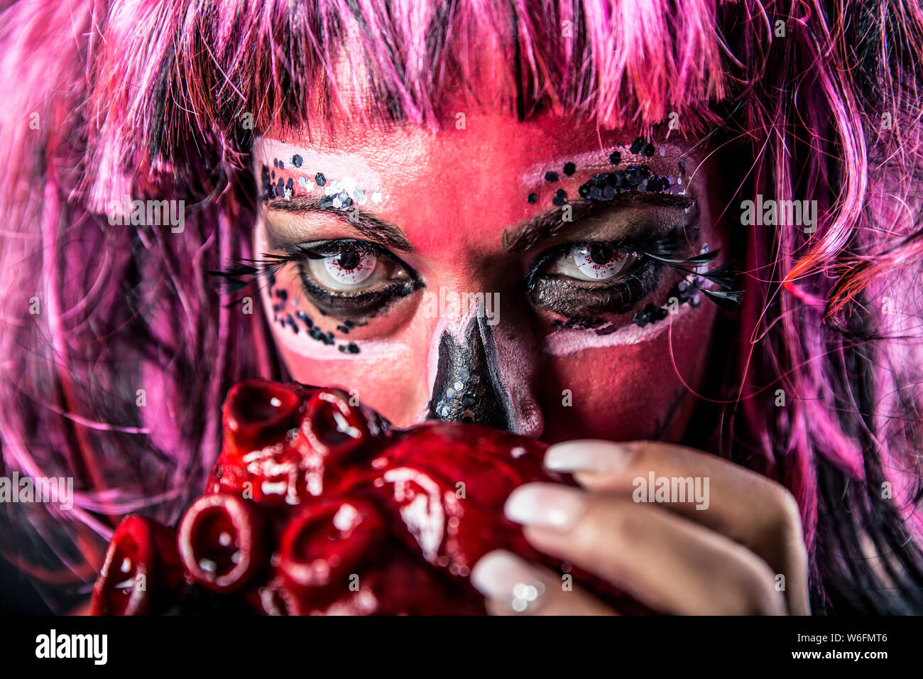 Nahaufnahme einer Frau mit Sugar Skull Make-up hält ein blutiges Herz vor ihrem Mund. Geringe Tiefenschärfe. Stockfoto