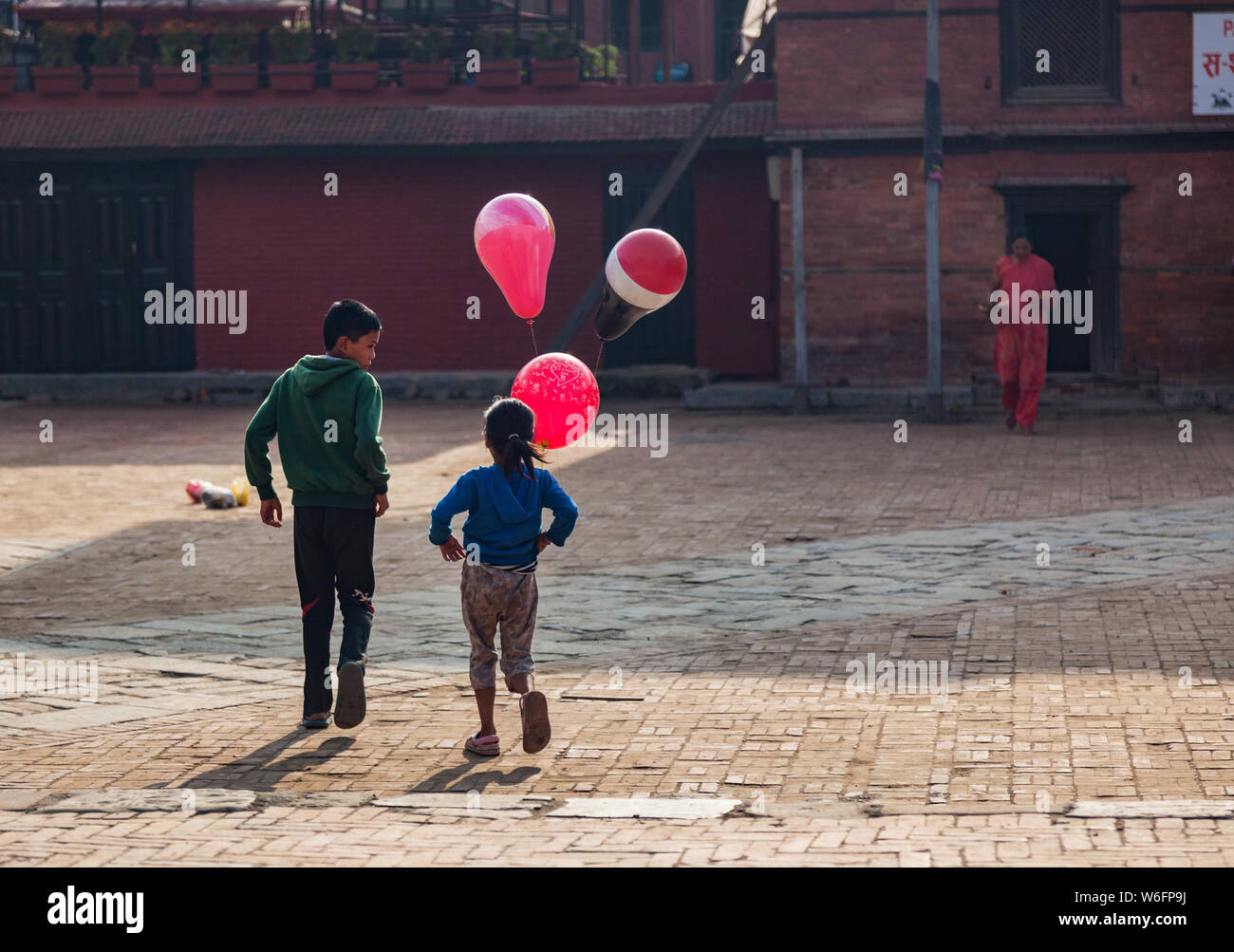 Jungen und Mädchen mit rosa Luftballons zu Fuß durch ein Quadrat in Kathmandu, Nepal. Stockfoto