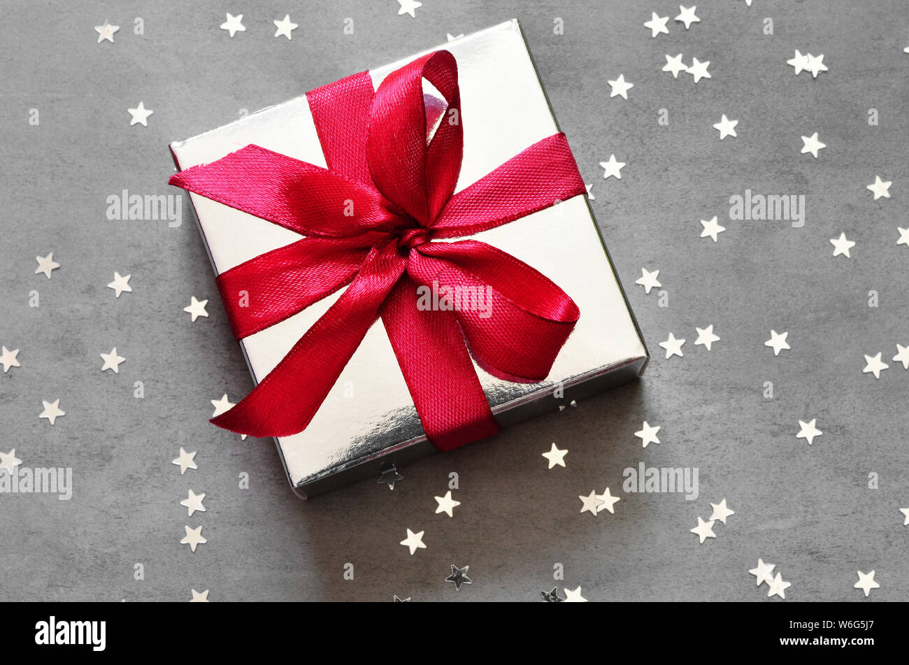 Geschenkbox mit roter Schleife auf grauem Hintergrund mit Stern. Ansicht von oben. Stockfoto