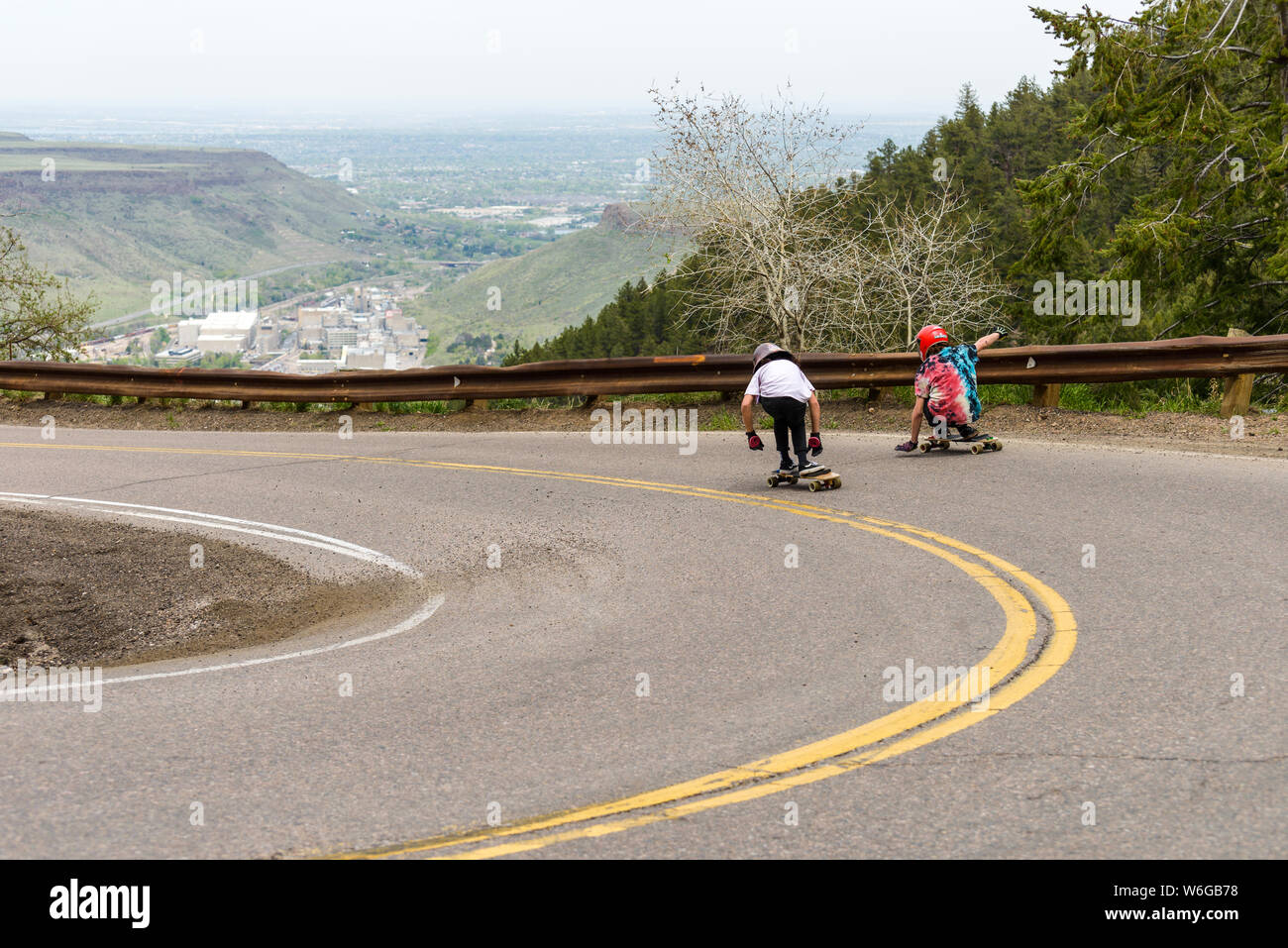 Longboarden den Berg hinunter Straße - Zwei Skateboarder, Kreuzfahrt eine steile und kurvenreiche Bergstrasse in Lookout Mountain, Golden, CO, USA. Stockfoto