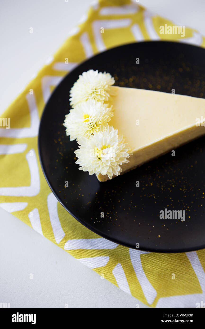 Cremige Käsekuchen mit weißen Blumen auf einem gelben Serviette geschmückt. Stockfoto
