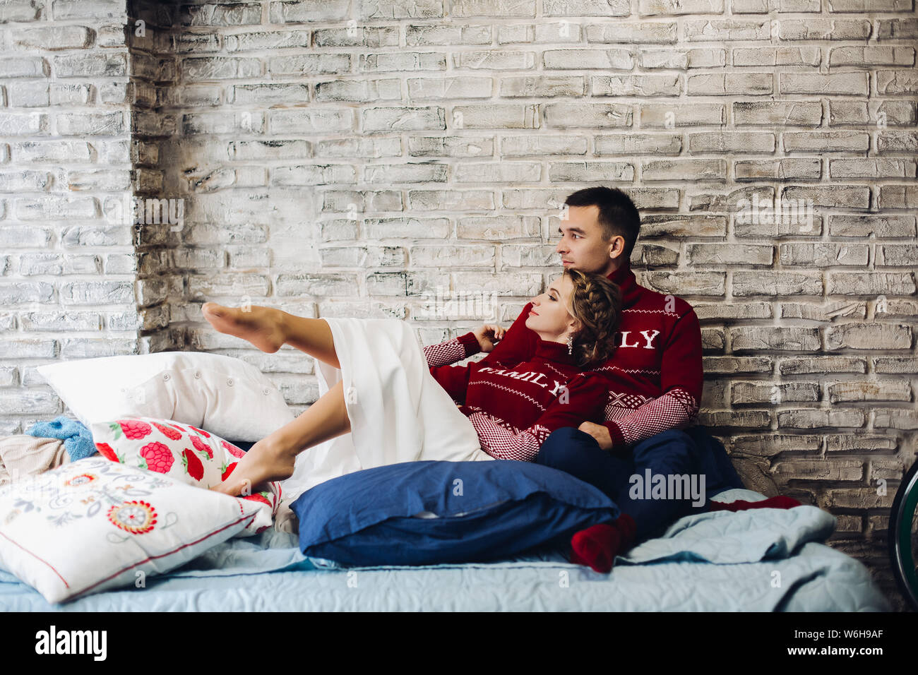 Paar rot weihnachten Jumper Küssen von Kissen umgeben. Stockfoto