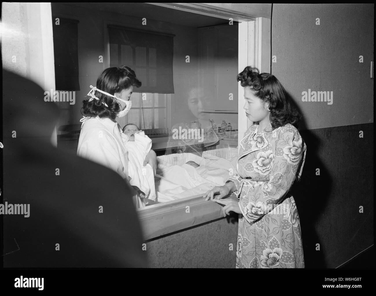 Herz Berg Relocation Center, Heart Mountain, Wyoming. Frau Mari Yoshida schaut sie Baby thro. . .; Umfang und Inhalt: Der vollständige Titel für dieses Foto liest: Herz Berg Relocation Center, Heart Mountain, Wyoming. Frau Mari Yoshida schaut Ihr Baby durch die Platte Glas Fenster des Kindergartens, als Krankenschwestern Adjutant Nobuko Hirashima zurück in seiner Krippe nach der Fütterung. Stockfoto