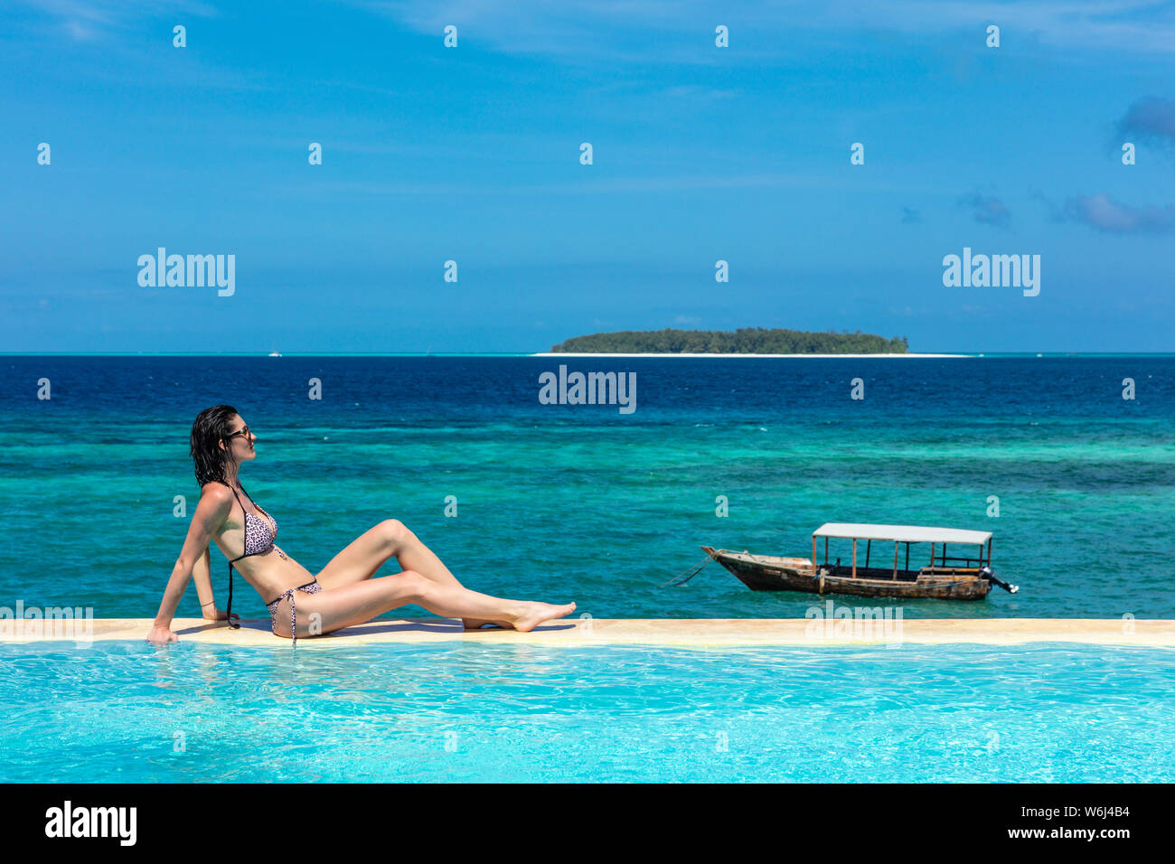 Eine kaukasische Frau genießen Ferien Sonnenbaden auf ein Infinity Pool direkt am Meer, mit Blick auf den Ozean idian Muyuni in Unguja aka Insel Sansibar Tansania Ostafrika Stockfoto
