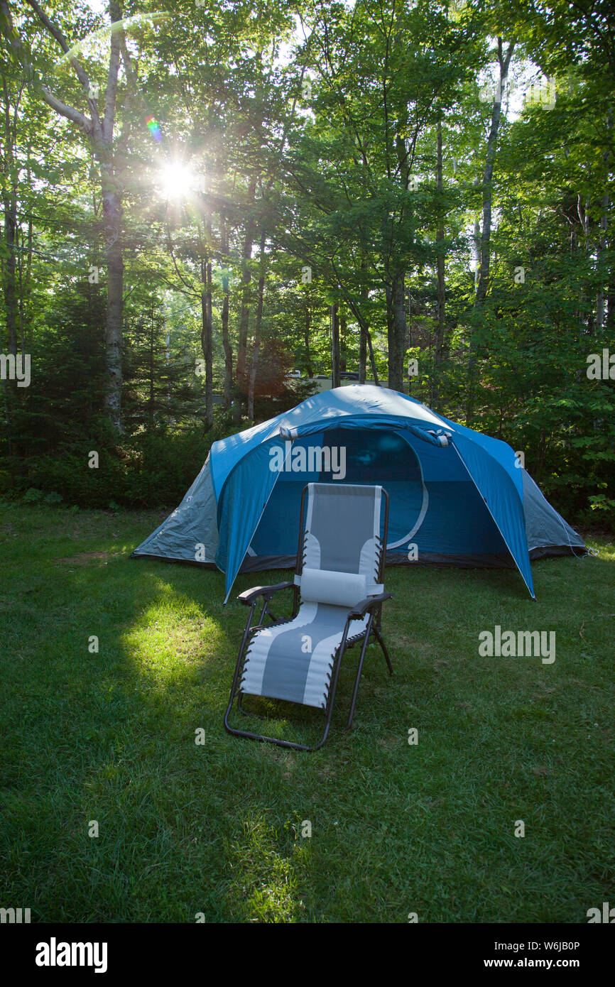 Blaues Zelt auf einem Campingplatz mit einem leeren Stuhl zum Entspannen vor es mit einer Sonne flare durch den Wald Stockfoto