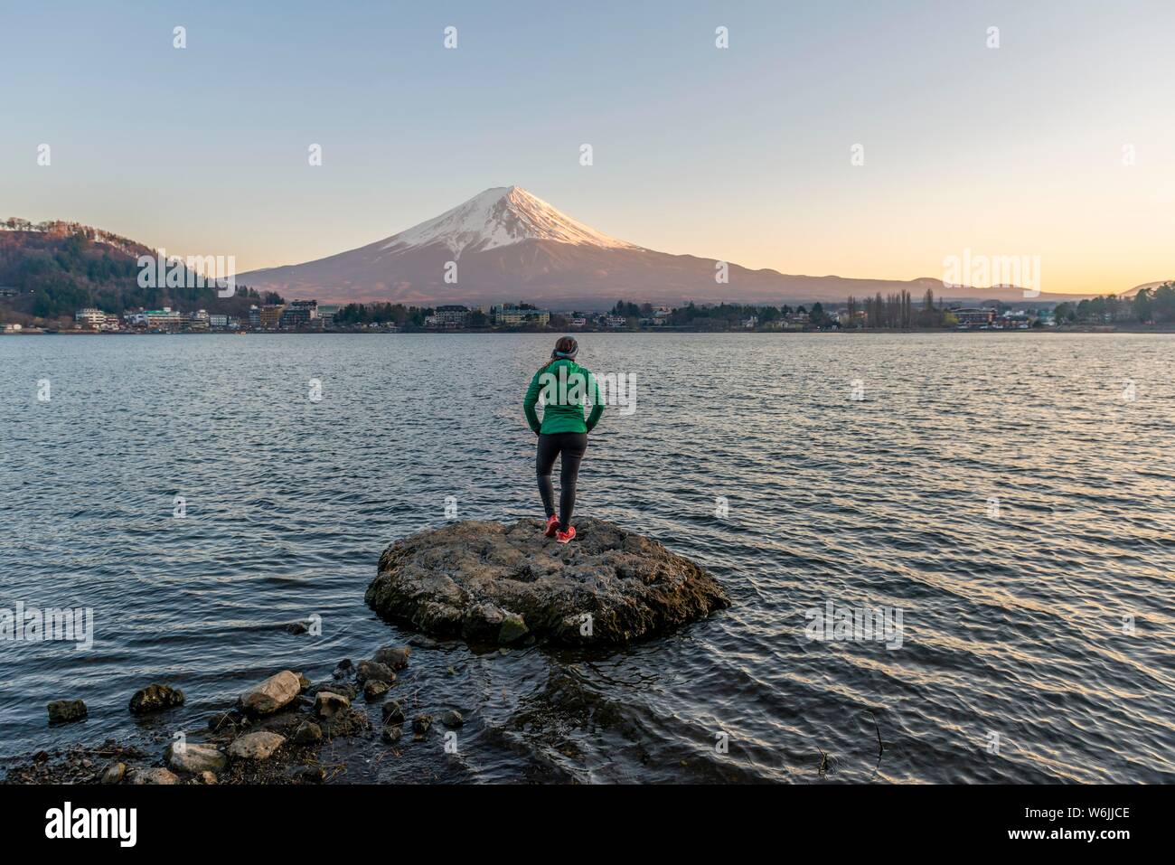 Abendstimmung, junge Frau auf einem Stein im Wasser und der Blick in die Ferne, Blick über Lake Kawaguchi, zurück Vulkan Mt. Fuji, Yamanashi Stockfoto