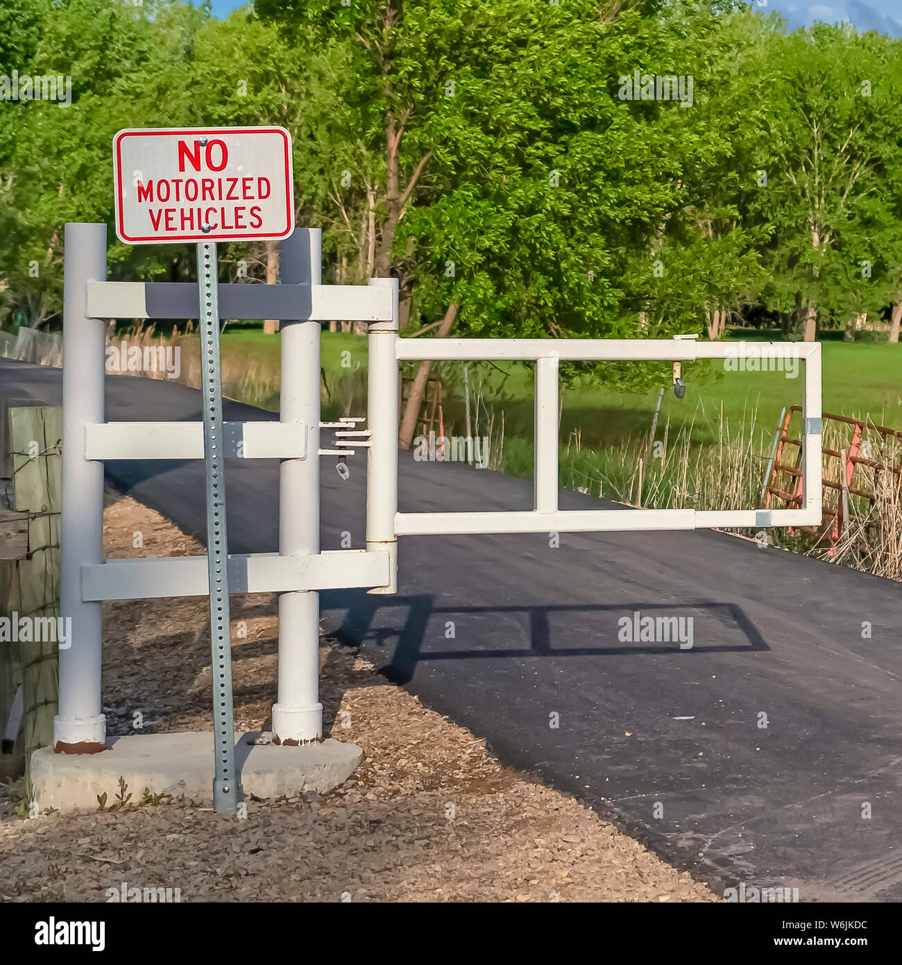 Quadrat Gestell weiß Tor und Schild auf einer schmalen Straße mit Wiese und Bäumen Hintergrund Stockfoto