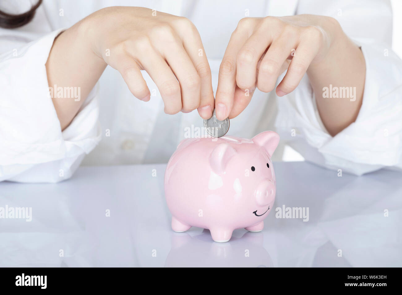 Weibliche hand Amicana Münzen und ein Viertel in ein Sparschwein auf weißem Hintergrund Stockfoto