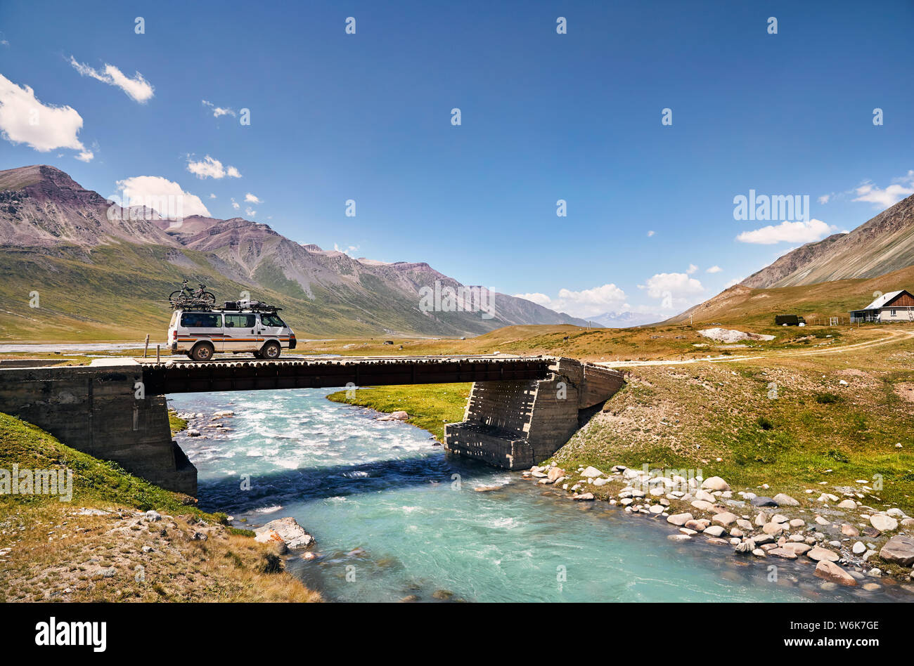 Weiß van mit dem Fahrrad auf dem Dach, überquert den Fluss über eine Brücke in den Bergen in Kirgisistan Stockfoto