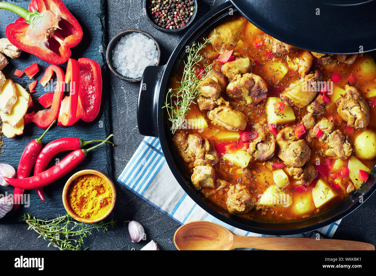 Close-up Chicken Curry mit Kartoffel, gehackten roten Paprika, Gewürze in einem schwarzen Keramik pan, Zutaten im Hintergrund, von oben betrachten Stockfoto