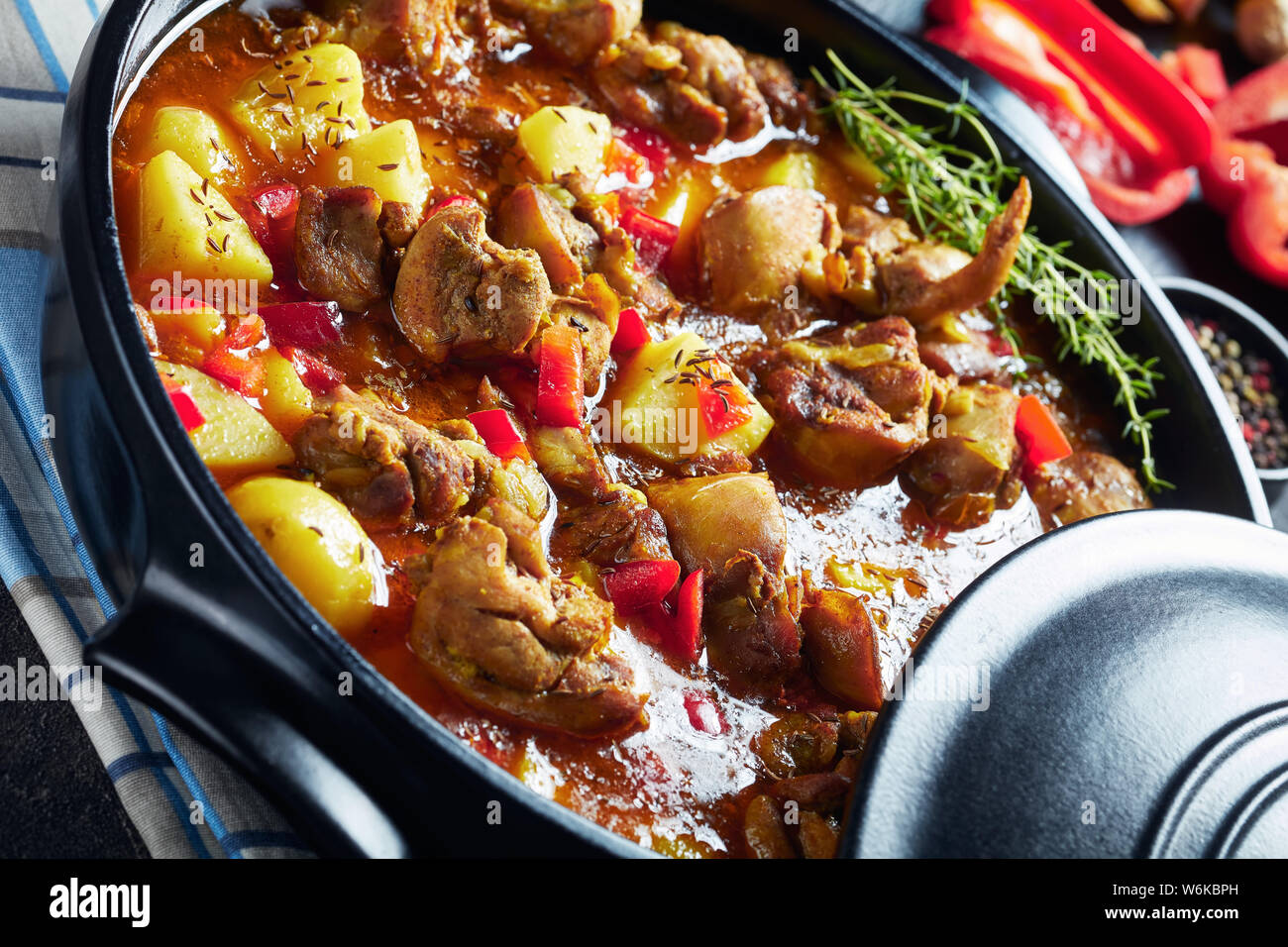 Close-up Chicken Curry mit Kartoffel, Paprika, Gewürze in einem schwarzen Keramik pan, Zutaten im Hintergrund, von oben betrachten, Makro Stockfoto
