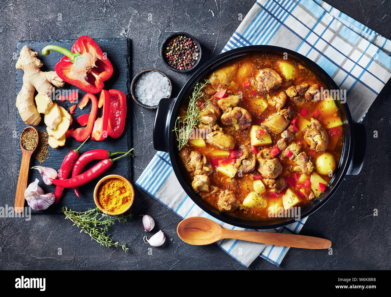 Chicken Curry mit Kartoffel, gehackten roten Paprika, Gewürze in einem schwarzen Keramik pan, Zutaten im Hintergrund, von oben betrachten, flatlay Stockfoto