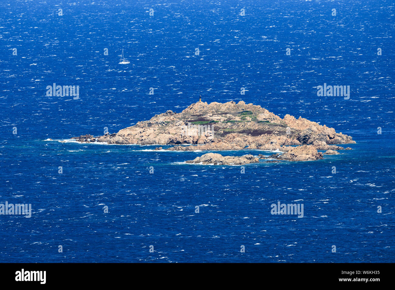 Ansicht von oben, atemberaubenden Blick auf rauer See mit einer kleinen felsigen Insel und ein Segelboot im Hintergrund. Sardinien, Italien. Stockfoto