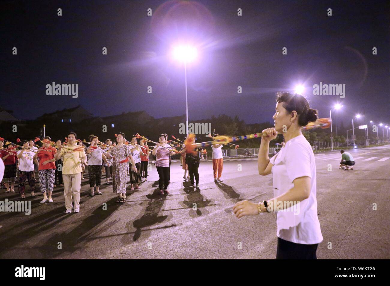 ------ Ältere Anwohner tanzen zu Musik mit Bambus Stäbe auf einem Platz in Minhang district, Shanghai, China, 4. August 2017. Junge techies Tak Stockfoto