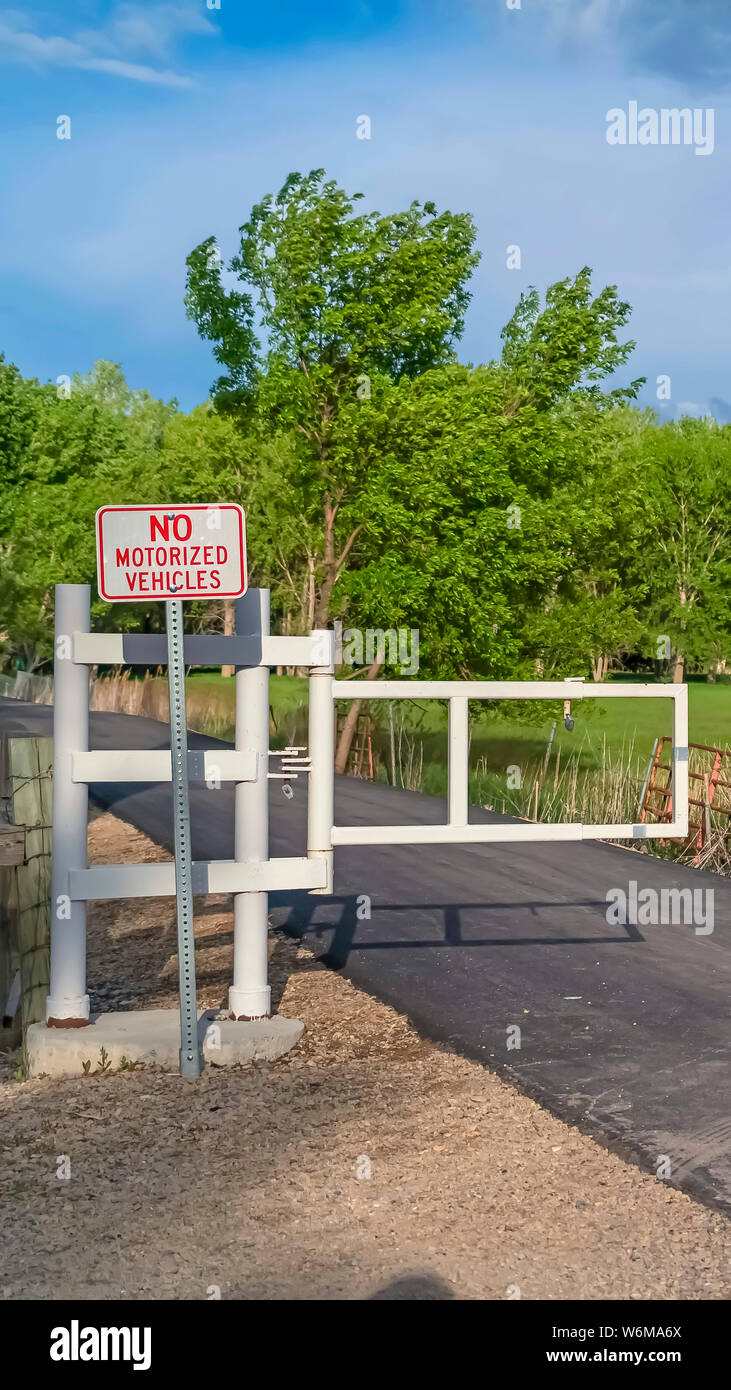 Vertikale weiße Tor und Schild auf einer schmalen Straße mit Wiese und Bäumen Hintergrund Stockfoto