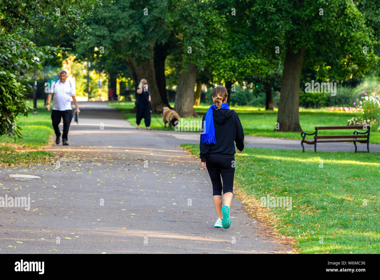 Northampton GROSSBRITANNIEN. 2. August 2019. Wetter. Einen warmen, sonnigen Morgen Für einige Übung im oberen Teil von Abington Park, eine junge Dame geht weg in die langen Schatten durch die niedrige Sonne verursacht, Kredit: Keith J Smith./Alamy leben Nachrichten Stockfoto