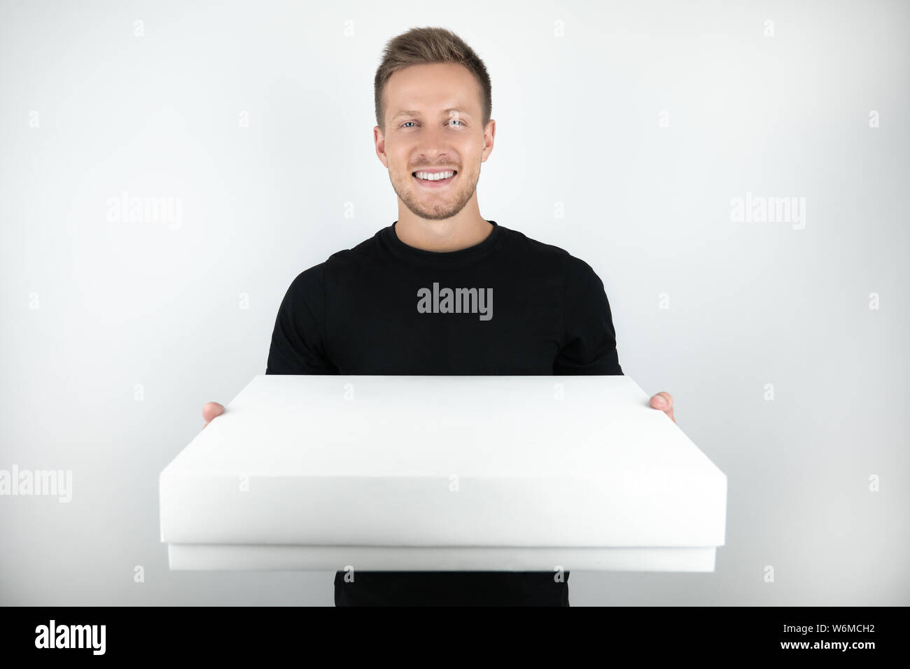 Hübscher junger Mann mit schwarzen T-Shirt holding Paket im Plastiketui für Lieferung auf isoliert weißer Hintergrund Stockfoto