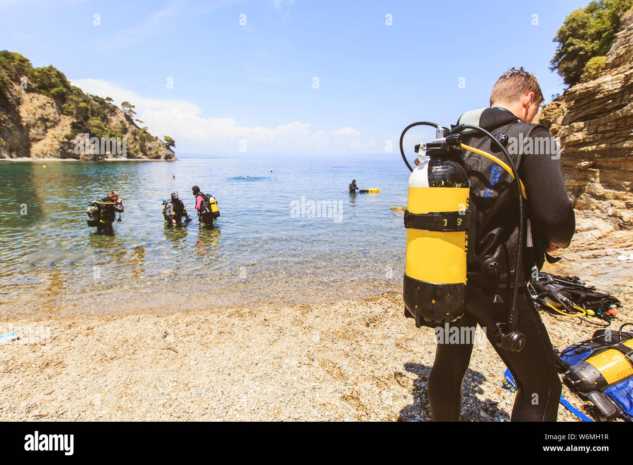 Ansicht der Rückseite des Scuba diver Mann mit Sauerstoff tank Vorbereitung zum Tauchen. Gruppe von Tauchern am Meer im Hintergrund. Sommer extreme Aktivität. Stockfoto