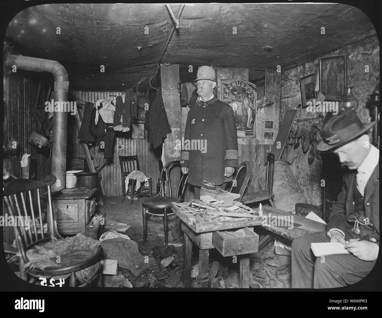 Zwei Beamte der Stadt New York Tenement House Abteilung untersuchen einen übervollen Keller Wohnzimmer, Ca. 1900 Stockfoto