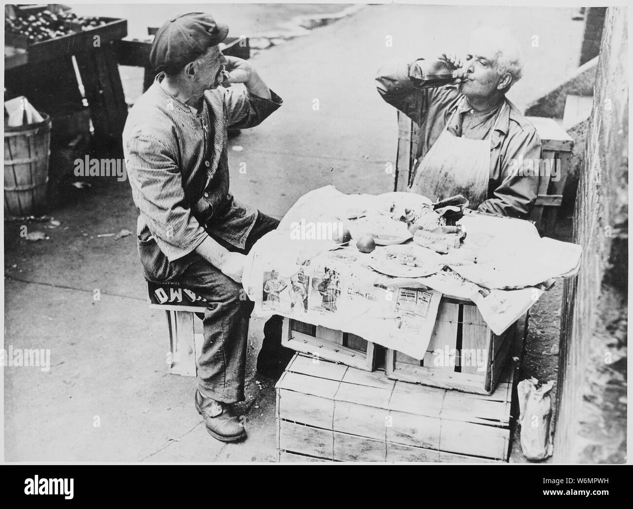 Zwei Straßenhändler die Zeit nehmen zum Mittagessen in einem behelfsmäßigen Tabelle der Holzkisten mit Zeitung, 08/1946 Stockfoto