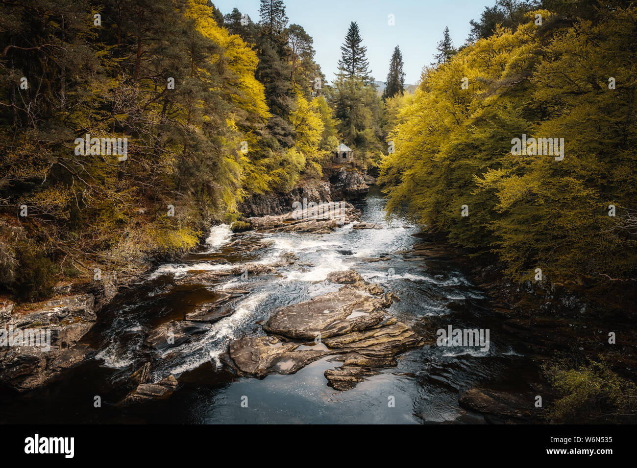 Goldenen Bäumen hängen über den Moriston River bei Invermoriston in Schottland mit einem kleinen Gebäude aus Stein in der Ferne Stockfoto