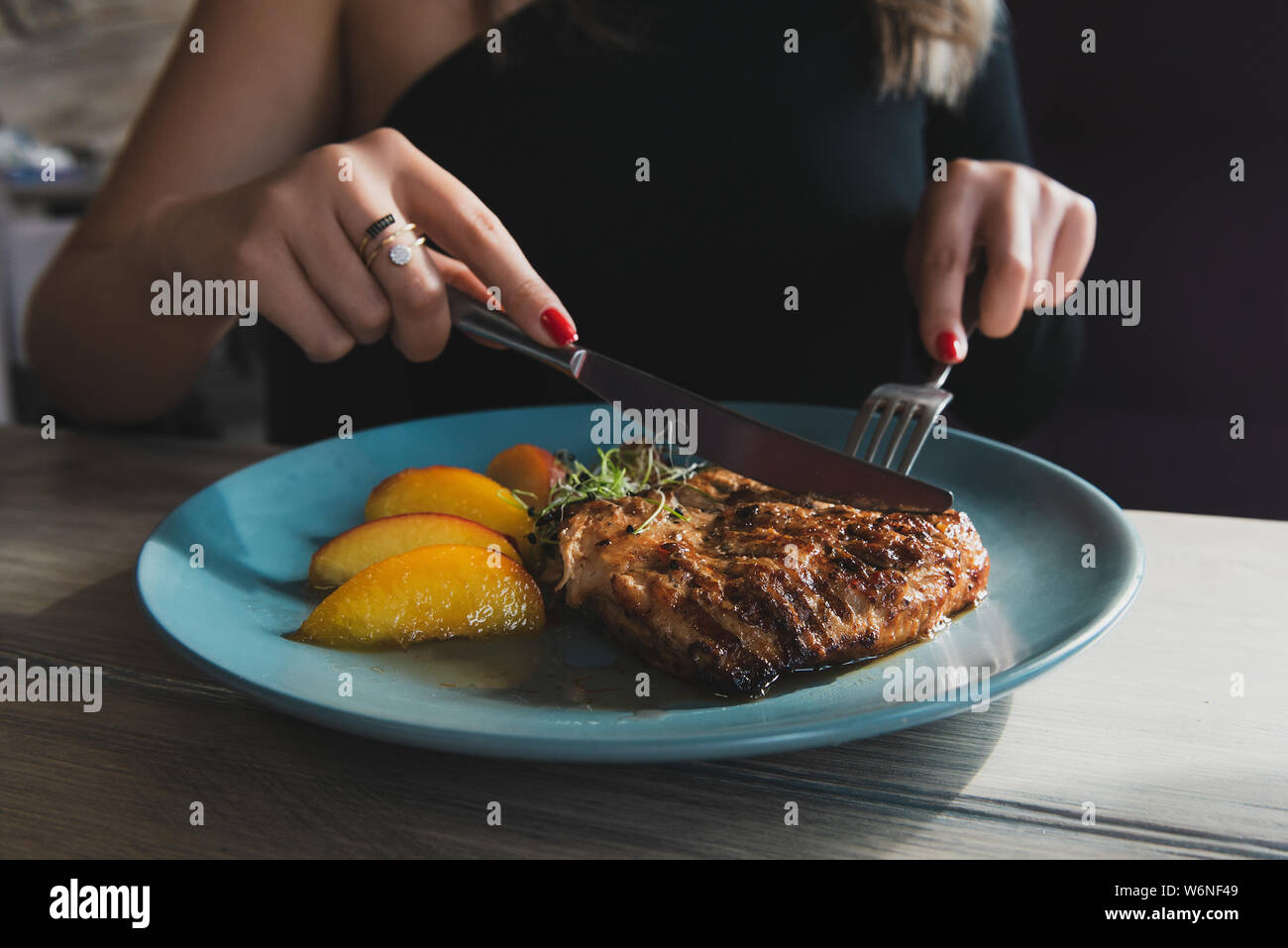 Mädchen Schnitte Saftig gegrillte Putensteak mit Messer und Gabel auf den türkisblauen Platte. Hähnchenfilet. Steak serviert mit karamellisiertem Pfirsich. Stockfoto