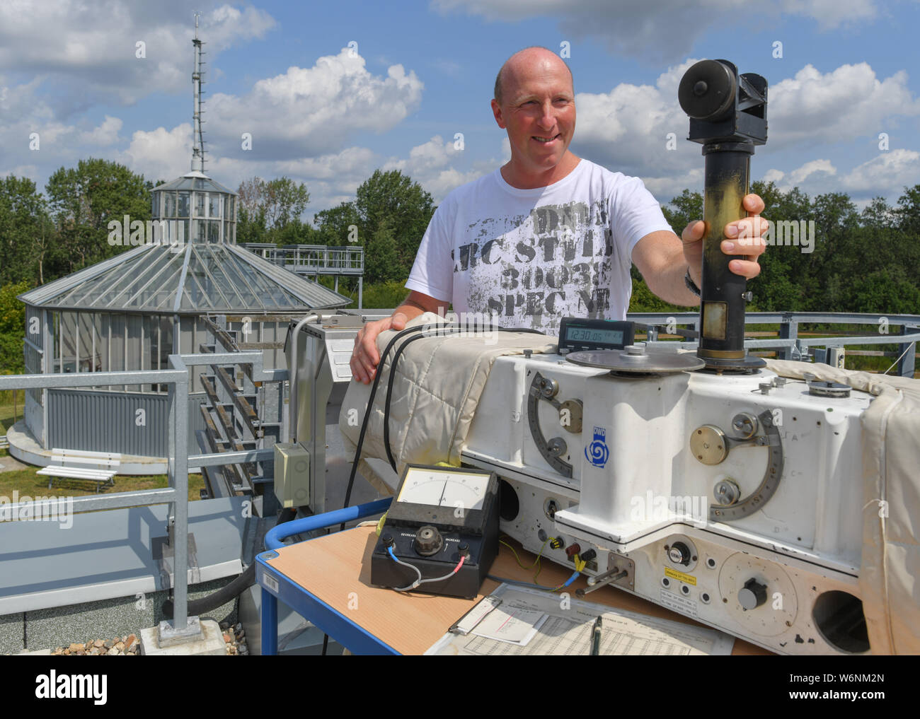 02. August 2019, Brandenburg, Lindenberg: Ingo Ortmann, meteorologische Techniker des Meteorologischen Observatoriums Lindenberg-Richard-Aßmann-Observatorium des Deutschen Wetterdienstes (DWD), arbeitet an einem Dobson Spektralphotometer für die Messung von Ozon. Im Hintergrund sehen Sie die historischen Winde Haus. Vor hundert Jahren, am 01.08.1919, dieser Winde Haus stellte den Weltrekord für große Höhen wetter Drachen. Zu dieser Zeit ein Wetter kite ein dünnes Stahlseil bis zu einer Höhe von 9750 Meter gezogen. Der Datensatz ist noch nicht gebrochen. Deutschlands erste aeronautische Warnung Dienst wurde gestartet Stockfoto