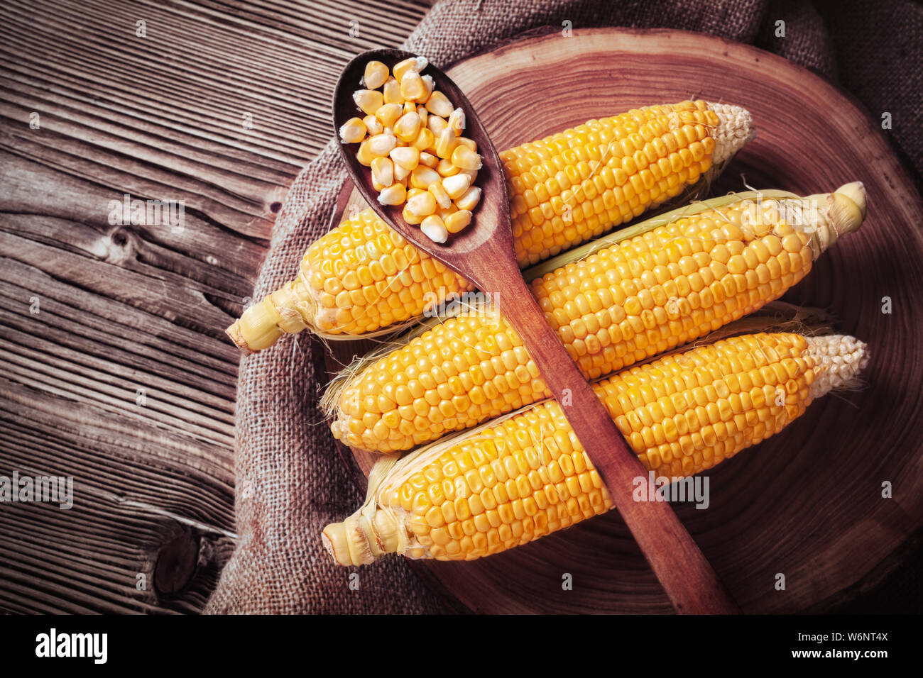 Frischen süßen Bio Hühneraugen auf Baum Slice auf Säcken. Maiskörner in hölzernen Löffel auf Kolben. Gesunde Ernährung Konzept. Stockfoto