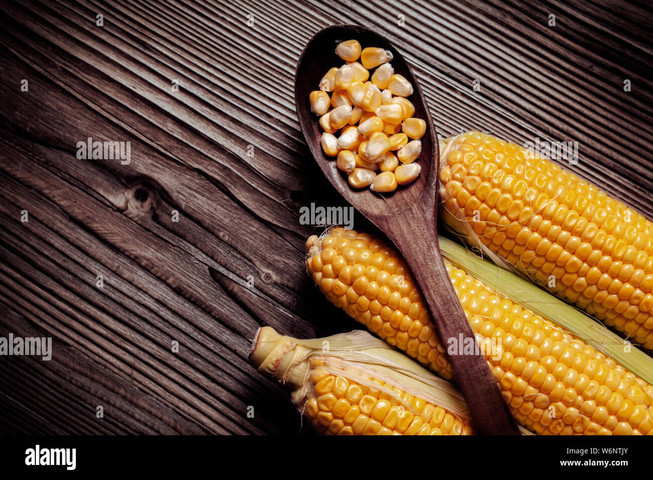 Maiskörner in hölzernen Löffel über frischen süßen Bio Hühneraugen auf Holz rustikal Tisch gelegt. Gesunde Ernährung Konzept. Stockfoto