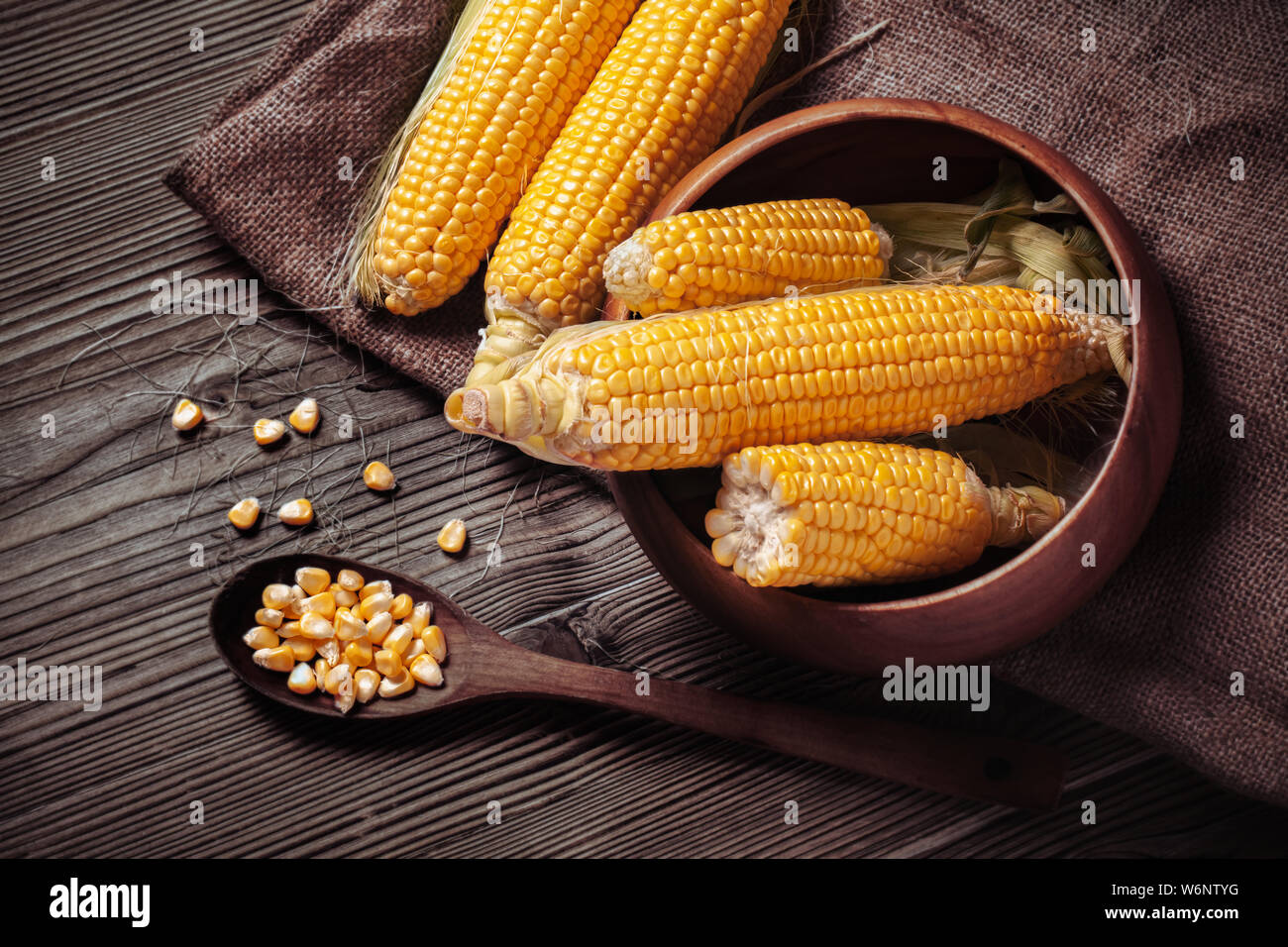 Schale mit frischen süßen Bio Mais auf Holztisch. Mais auf Säcken. Maiskörner in hölzernen Löffel auf rustikalen Holztisch in der Küche. Stockfoto