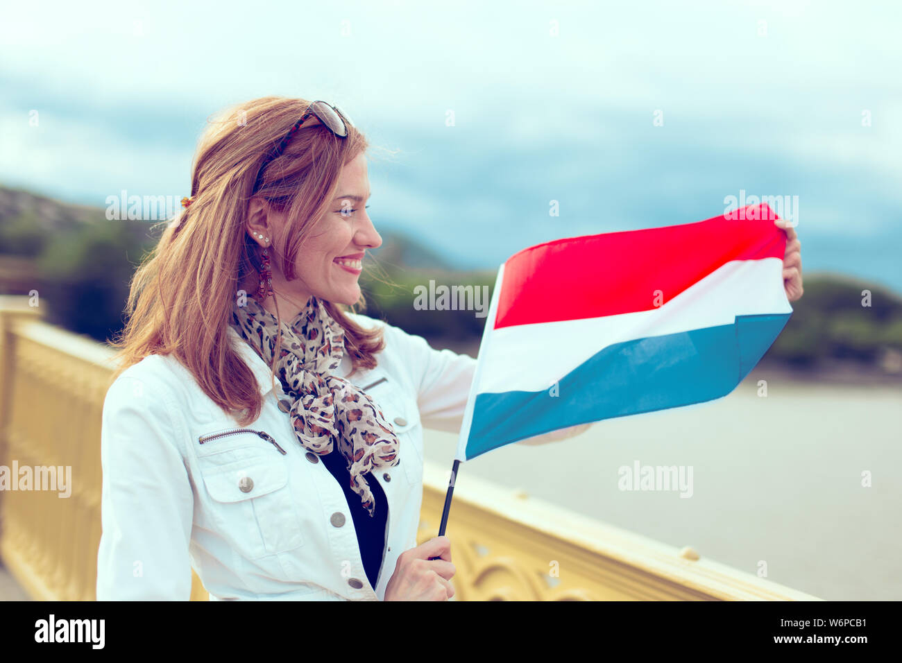 Glückliche Junge kaukasier Frau stretching niederländischer Flagge auf der Brücke Stockfoto