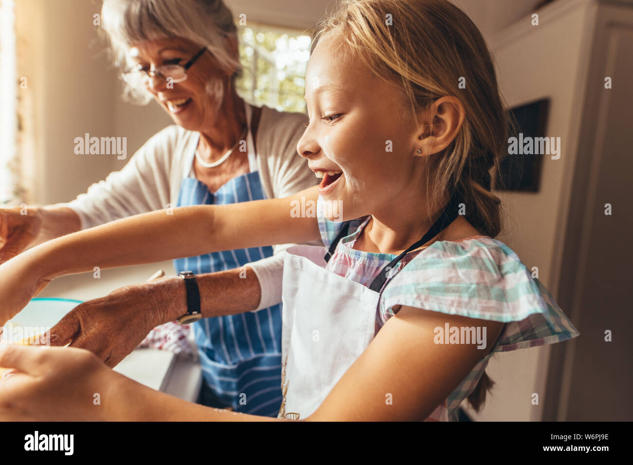 Oma und Kind Spaß Kochen in der Küche. Glückliches Mädchen lernen Essen mit Schürze tragen ihrer Großmutter zu kochen. Stockfoto
