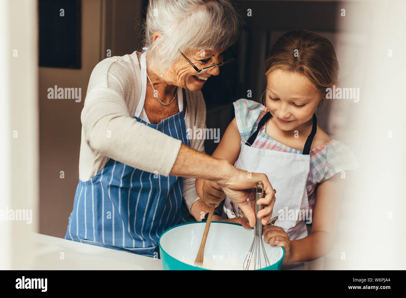 Ältere Frau Lehre ein Kind Teig für Kuchen zu machen. Lächelnde Großmutter und Mädchen mischen Teig in eine Schüssel geben. Stockfoto