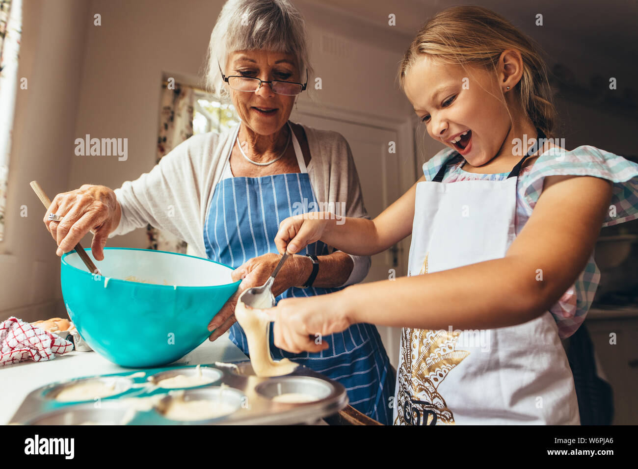 Kleines Mädchen lernen cup cakes mit ihrer Großmutter zu machen. Aufgeregt Mädchen gießen Kuchenteig in Cup Cake formen. Stockfoto