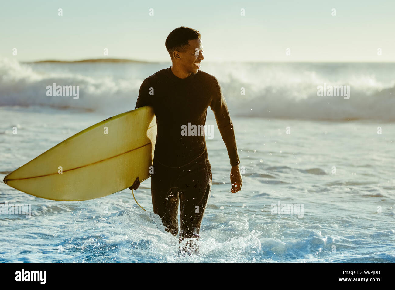 Lächelnden jungen Mann mit Surfbrett am Strand. Afrikanische Mann aus dem Ozean nach Wasser surfen. Stockfoto
