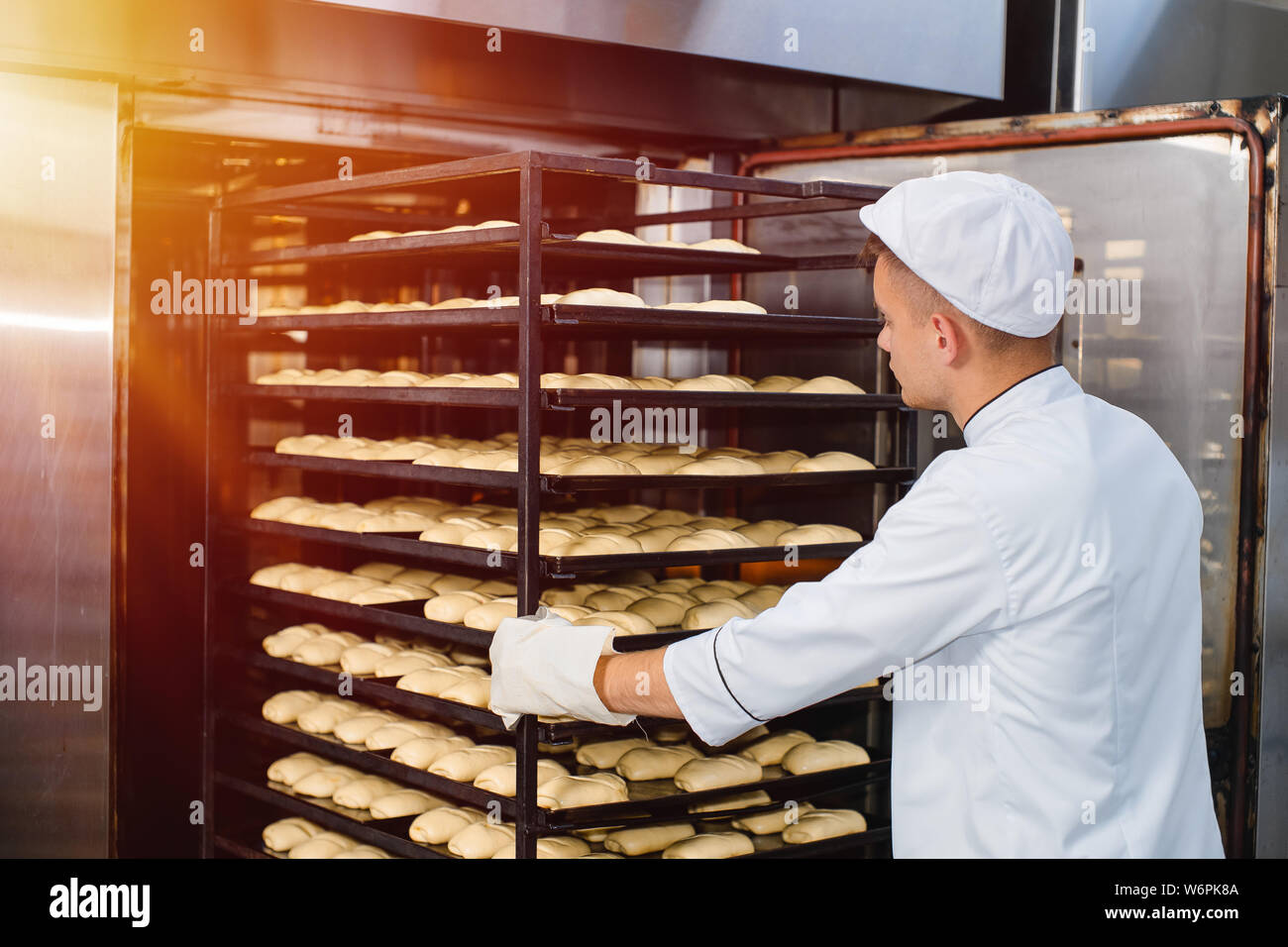 Ein Bäcker trägt einen Warenkorb mit einem Backblech mit rohen Teig in einen Backofen. industriellen Ofen in einer Bäckerei. Stockfoto