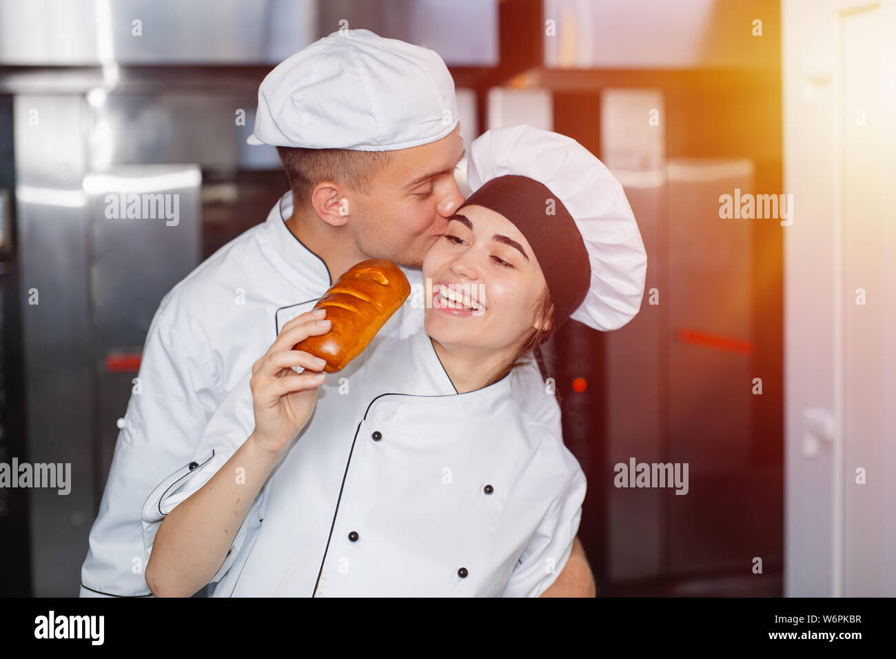 Junge Bäcker ein Mädchen Küsse auf die Wange in einer Bäckerei vor dem Hintergrund der Backofen. Stockfoto