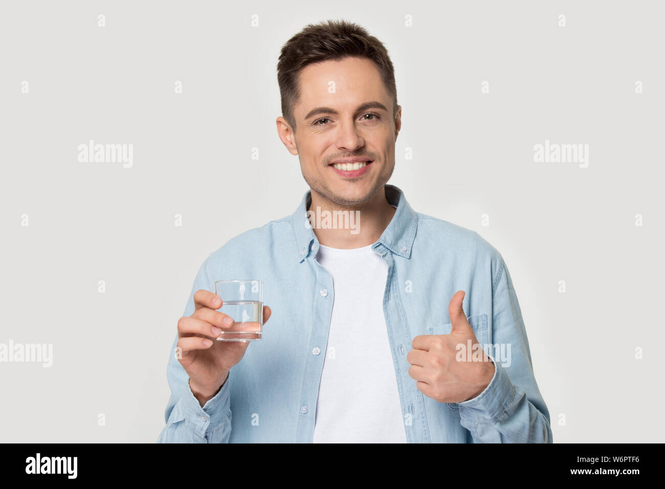 Gesundes Lächeln Mann hält Glas Wasser mit Daumen hoch Stockfoto