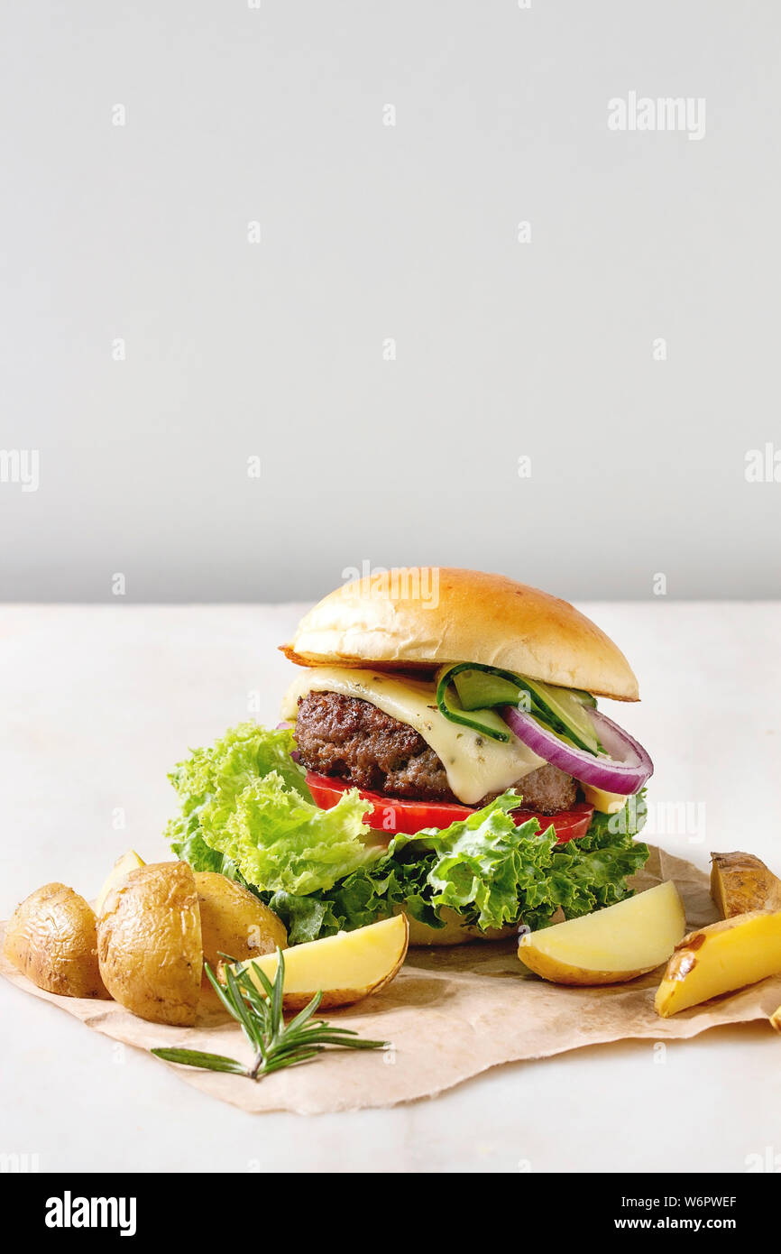 Hausgemachte Fast Food Burger classic Hamburger oder Cheeseburger mit Rindfleisch, Salat, Käse und Tomaten serviert auf Papier mit gebackenen Land Kartoffeln auf Weiß m Stockfoto