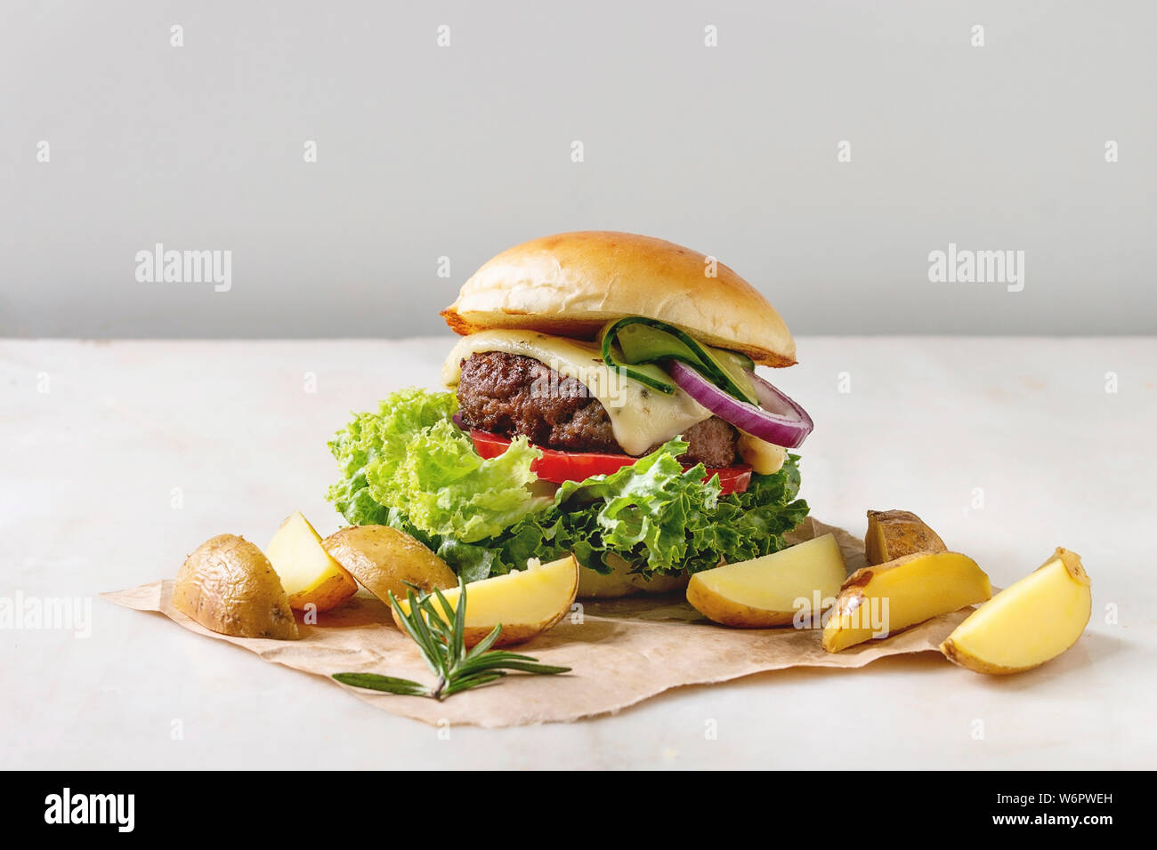 Hausgemachte Fast Food Burger classic Hamburger oder Cheeseburger mit Rindfleisch, Salat, Käse und Tomaten serviert auf Papier mit gebackenen Land Kartoffeln auf Weiß m Stockfoto